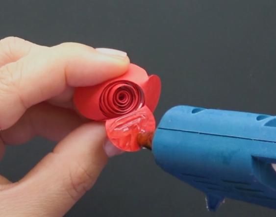 Securing the bottom of a rolled paper rose with hot glue