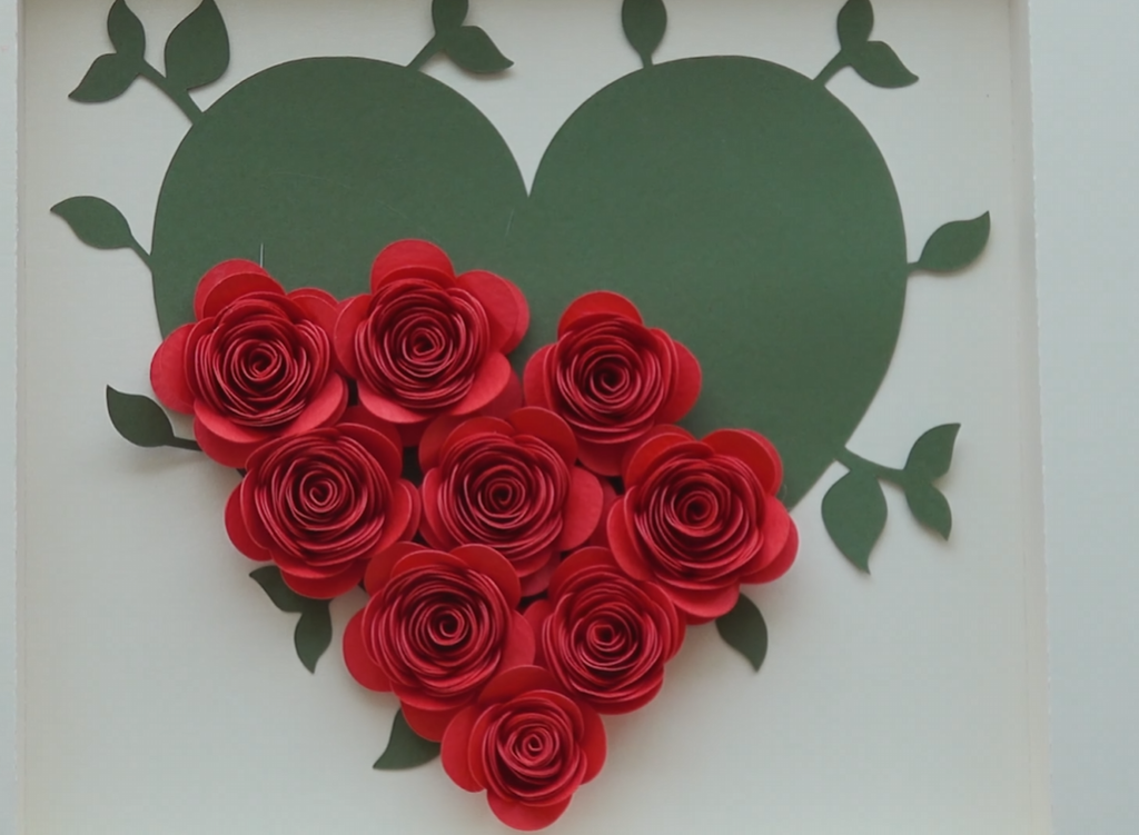 Arranging red rolled paper roses from the bottom of a green heart shape