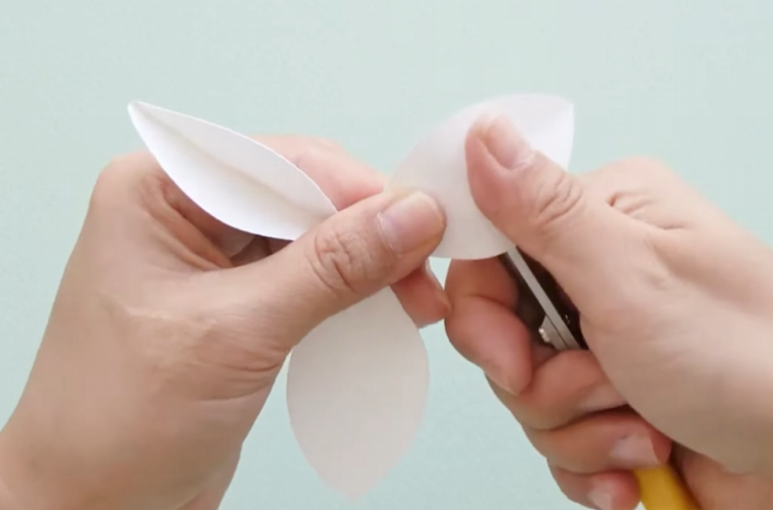 Curling white cardstock petals backward with scissors for a paper daffodil