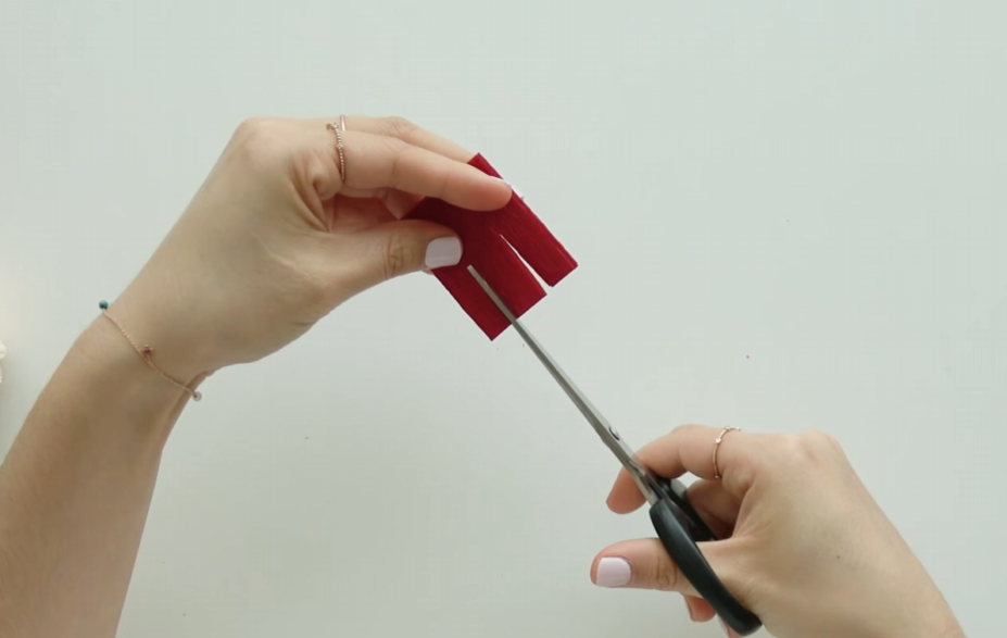 Cutting folded red crepe paper into three sections for carnation petals