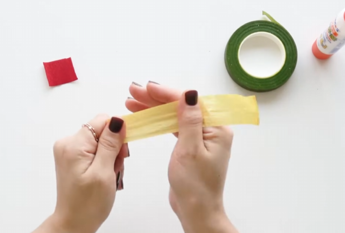 Hands stretching yellow crepe paper to prepare the center of a handmade Christmas poinsettia