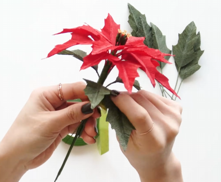 Attaching textured green leaves beneath the red petals of a handmade poinsettia