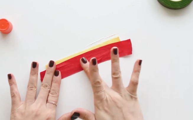Layering a red crepe paper strip beneath yellow paper to make realistic poinsettia stamens