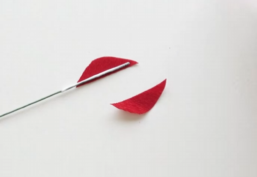 Attaching thin green floral wire to the edge of a curved red crepe paper petal