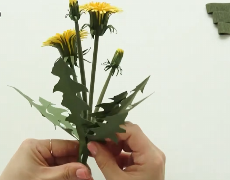 Arranging handmade paper dandelion flowers and leaves together on the stems