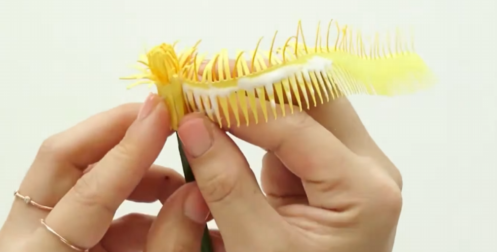 Rolling a fringed yellow paper strip around the flower stem to build the dandelion petals