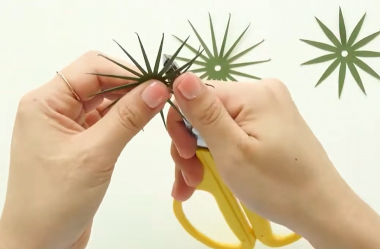 Shaping green cardstock sepals with scissors for the base of a paper dandelion