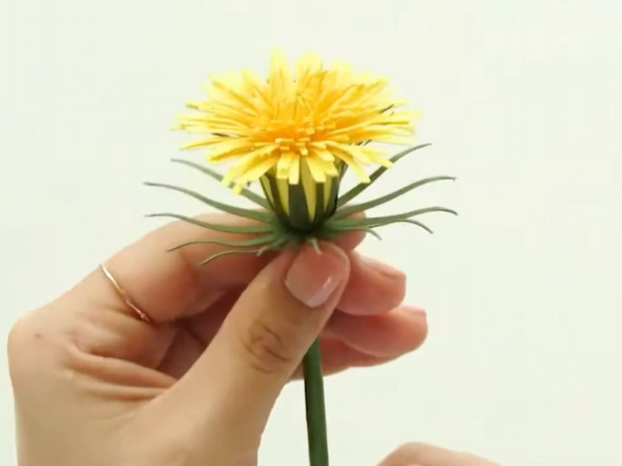 Finished yellow paper dandelion flower with green sepals wrapped around the base