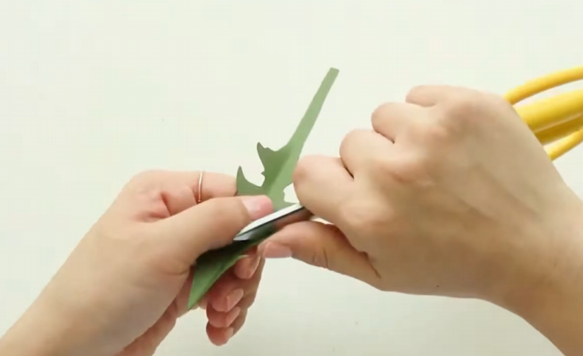 Curving the edges of a green cardstock dandelion leaf with scissors